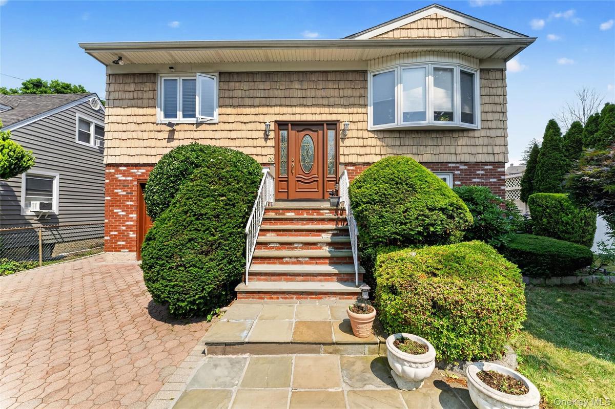 Front elevation featuring shake siding, brick accents, a wood-finish entry door, a bay window, and a paver driveway