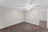 Spacious room featuring neutral wall paint, brown carpeting, and a ceiling fan with light fixture