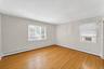 Spacious interior room featuring wood-finish flooring, light-toned walls, two windows with blinds, and baseboard heating