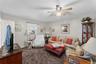Carpeted living area featuring a ceiling fan with light fixture, window with blinds, and white painted walls