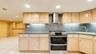 Kitchen featuring light wood-finish cabinetry, stone countertops, a stainless steel range with double ovens, a stainless steel range hood, and an unde