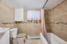 Bathroom featuring floor-to-ceiling tile, decorative mosaic accent band, white wall-mounted cabinet, window, and a built-in bathtub with shower