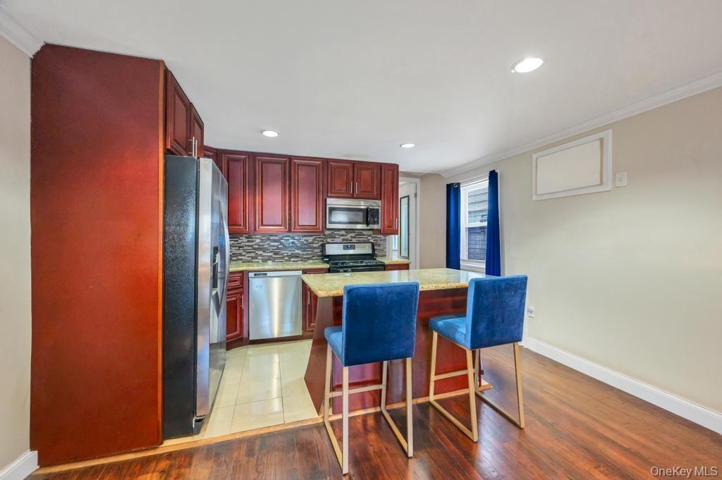 Kitchen featuring dark wood cabinetry, stainless steel appliances, a multi-tone tile backsplash, and a central island with a light-toned countertop