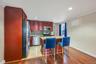 Kitchen featuring dark wood cabinetry, stainless steel appliances, a multi-tone tile backsplash, and a central island with a light-toned countertop