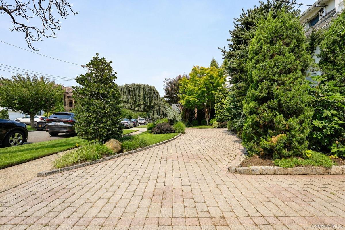 Paver driveway with a multi-level design, bordered by lush landscaping and mature trees