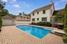 Curved inground pool with a diving board, surrounded by extensive paver patio