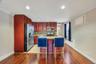 Open-concept kitchen featuring wood-finish cabinetry, stainless steel appliances, a multi-tone tile backsplash, and a central island with a light-colo