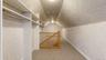 Attic space featuring built-in white shelving, hanging rods, light beige textured walls, and light beige carpet flooring