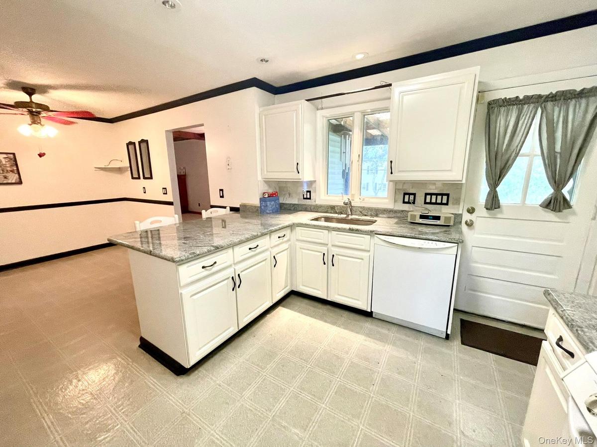 Open-concept kitchen featuring white cabinetry, light-toned granite-style countertops, and a built-in dishwasher