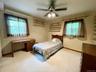 Carpeted room featuring a ceiling fan with integrated lighting, two windows with brown sheer curtains, and multiple wall-mounted shelving units