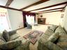 Living area featuring exposed wood beams, a prominent fireplace with a wood mantle and stone hearth, and light-colored carpeting