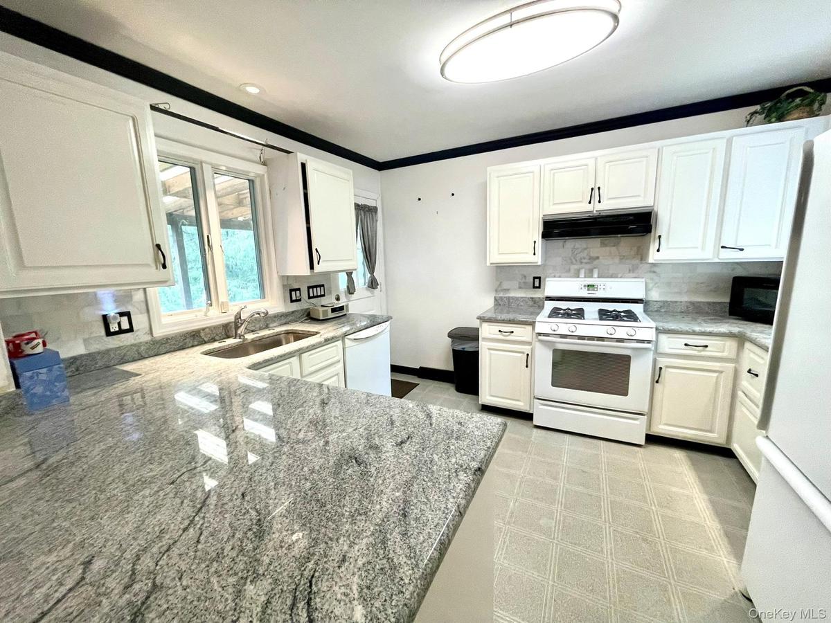 Kitchen featuring light-toned countertops, white cabinetry with dark hardware, a white range, a stainless steel sink, and a tiled backsplash