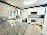 Kitchen featuring light-toned countertops, white cabinetry with dark hardware, a white range, a stainless steel sink, and a tiled backsplash