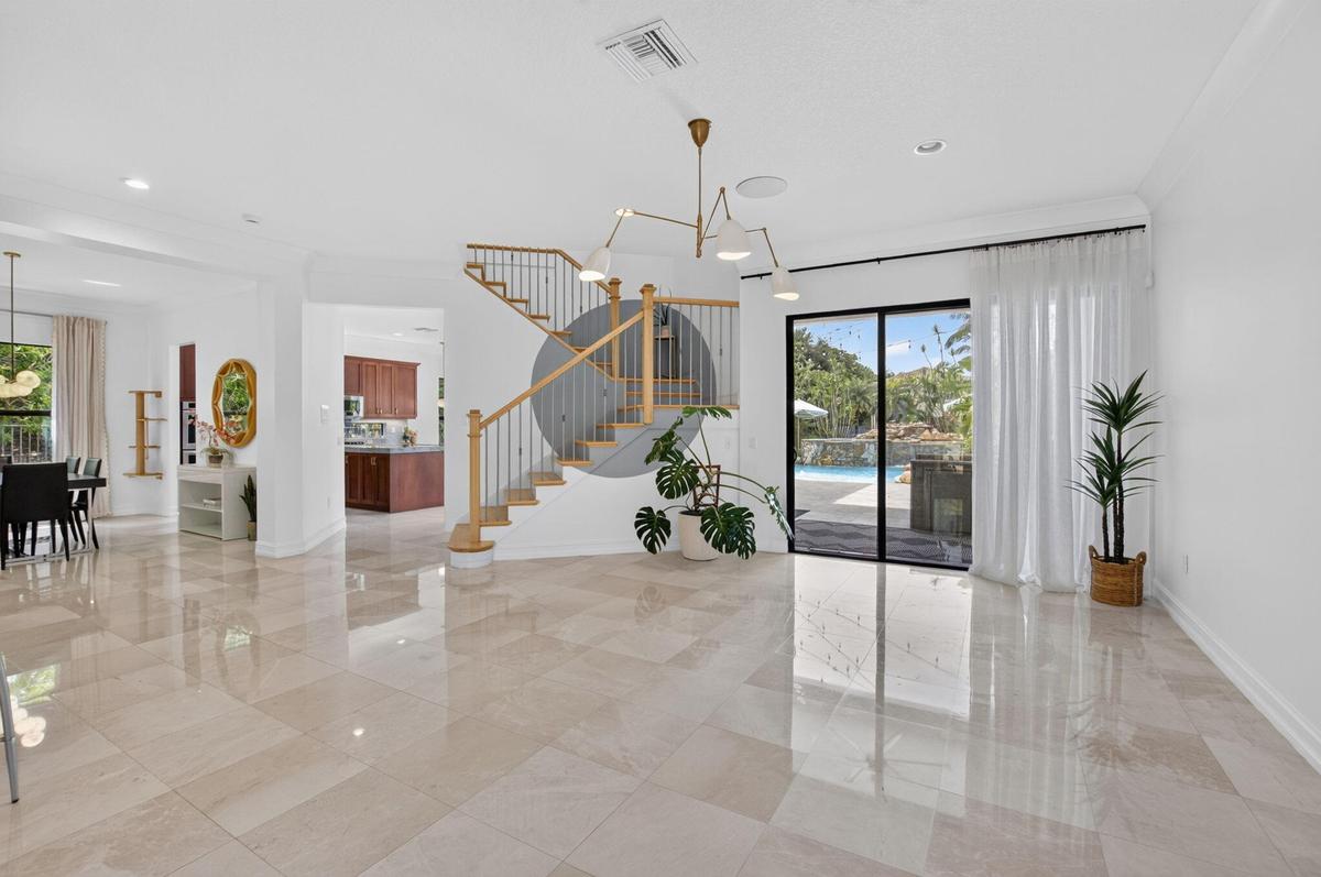 Expansive main living area featuring polished tile flooring, a contemporary chandelier, a staircase with wood newel posts and metal spindles, and larg