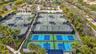 Expansive tennis and pickleball courts featuring perimeter fencing, spectator shelters, and court lighting