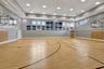 Indoor sports court featuring wood-finish flooring with court markings, dual basketball hoops, recessed ceiling lighting, and upper-level windows