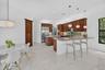 Spacious kitchen featuring warm wood cabinetry, stainless steel appliances, a multi-level island with seating, a window backsplash, and pendant lighti