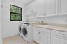 Dedicated utility room featuring white shaker-style cabinetry, a built-in utility sink, light-toned countertops, and a window providing natural light