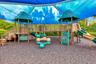 Playground structure with multiple slides and climbing elements, set on a dark-toned impact-absorbing surface