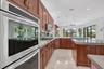 Gourmet kitchen featuring stainless steel double ovens, rich wood cabinetry with gold-tone hardware, light-toned stone countertops, and recessed light