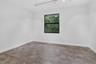 Spacious room featuring wood-finish flooring, white walls, and a black-framed window