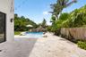 Expansive patio featuring light-toned natural stone pavers, a free-form swimming pool with a rock waterfall feature, tropical landscaping, and a bambo