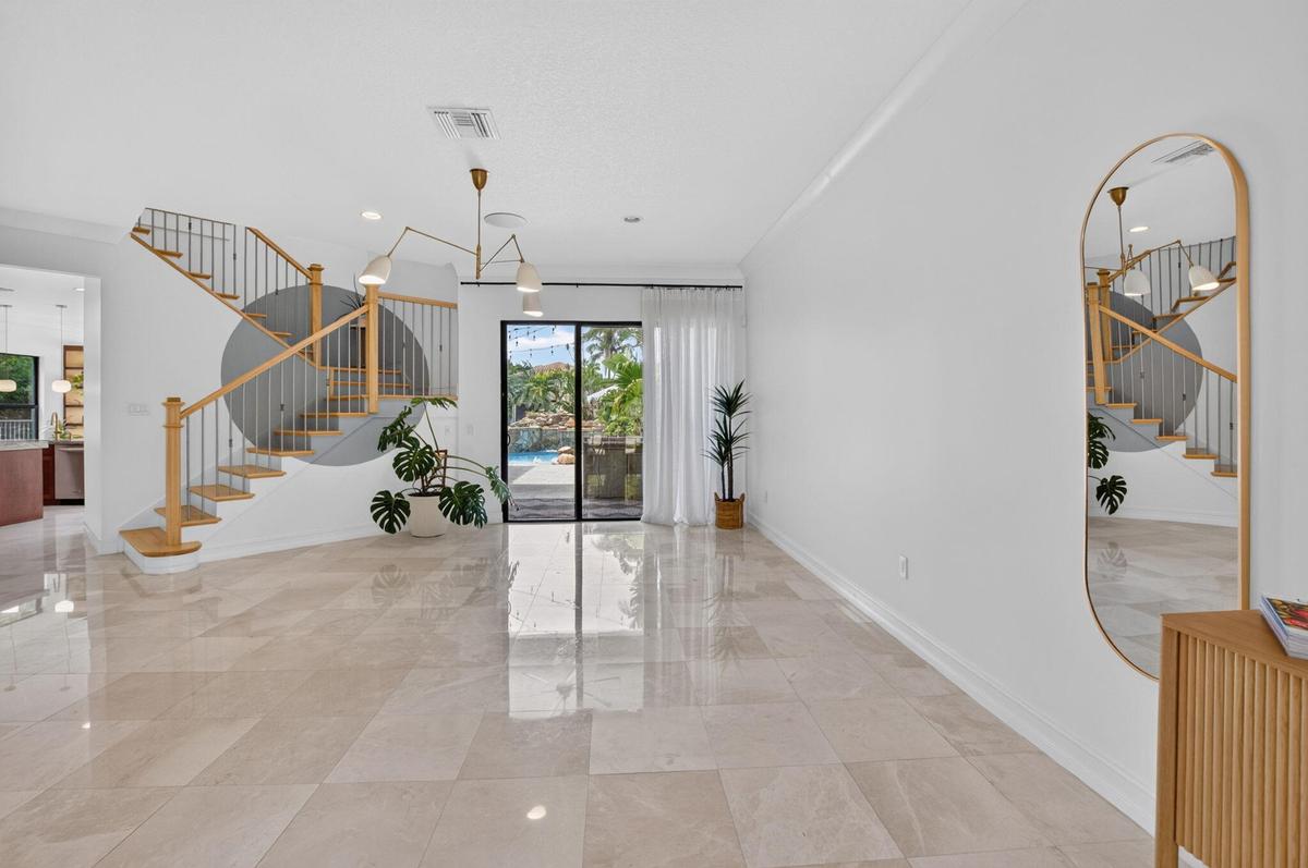 Spacious interior featuring large format tile flooring, a contemporary staircase with wood handrails, and an elegant multi-arm ceiling fixture
