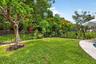 Spacious backyard featuring a lush lawn, mature trees, and a black wrought iron fence