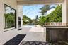 Outdoor living area featuring a built-in outdoor kitchen with stainless steel appliances, a spacious paved patio, and a swimming pool with a rock wate