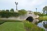 The Bridges entrance bridge featuring decorative street lamps, lush green landscaping, and reflective water