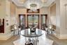 Entryway featuring three wood-paneled glass doors, a large central chandelier, and a decorative circular table with a dark, reflective surface