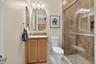 Bathroom featuring a single vanity with a granite-style countertop, wood-finish cabinetry, and a walk-in shower with tiled walls and a glass enclosure
