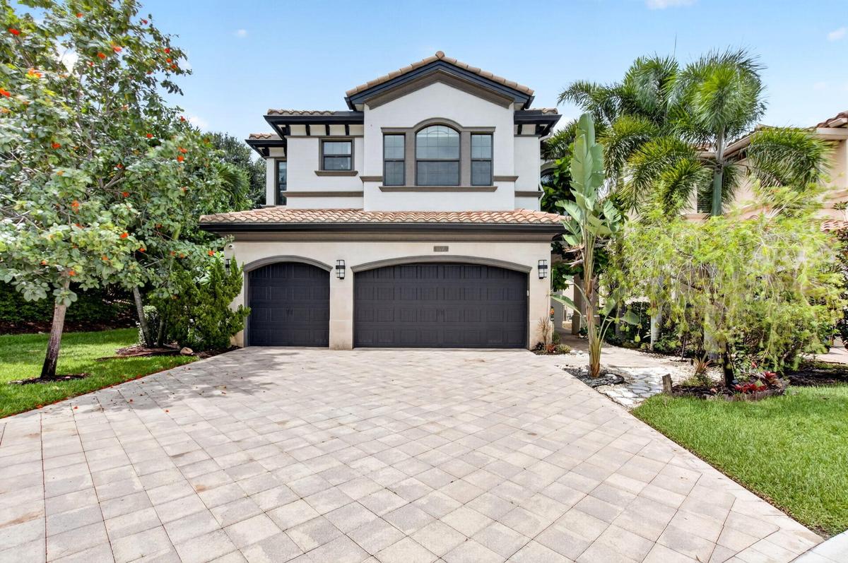 Stucco exterior featuring a tile roof, arched garage doors, and a paver driveway