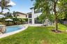 Expansive backyard featuring a curved swimming pool with a stone-clad waterfall, a large grassy area, mature trees, and a covered patio