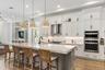 Kitchen with white cabinetry, large island, woven bar stools, and double wall ovens