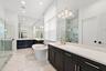 Primary bathroom with dual vanity, dark cabinetry, freestanding soaking tub, and glass shower