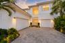Two-story home exterior with three-car garage and paver driveway at dusk