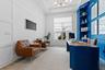 Home office with navy blue built-in desk and shelving, leather armchairs, and wall-mounted TV