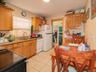 Kitchen featuring white appliances, ornamental molding, light tile patterned flooring, light stone counters, and brown cabinetry