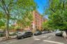 Brick multi-story residential building with multiple windows, featuring mature trees and street parking