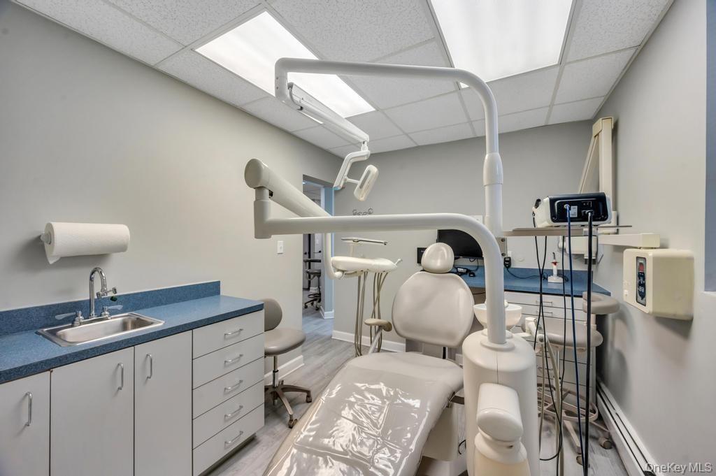 Exam room featuring light grey walls, suspended ceiling with integrated lighting, wood-finish flooring, and a built-in cabinetry unit with a sink and 