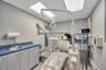 Exam room featuring light grey walls, suspended ceiling with integrated lighting, wood-finish flooring, and a built-in cabinetry unit with a sink and 