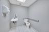 Commercial restroom featuring a wall-mounted sink, white toilet, and grab bars