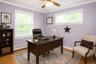 Spacious room featuring multiple windows with blinds, light wood-finish flooring, and a ceiling fan. AI Staged