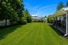 Expansive backyard featuring a lush lawn, mature trees, manicured shrubs, a privacy fence, and a covered porch with wood decking