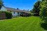 Expansive lawn with a covered deck, mature perimeter plantings, and a wooden privacy fence