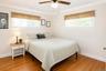VIRTUALLY STAGED. Bright bedroom featuring wood-finish flooring, two windows, and a ceiling fan with integrated lighting