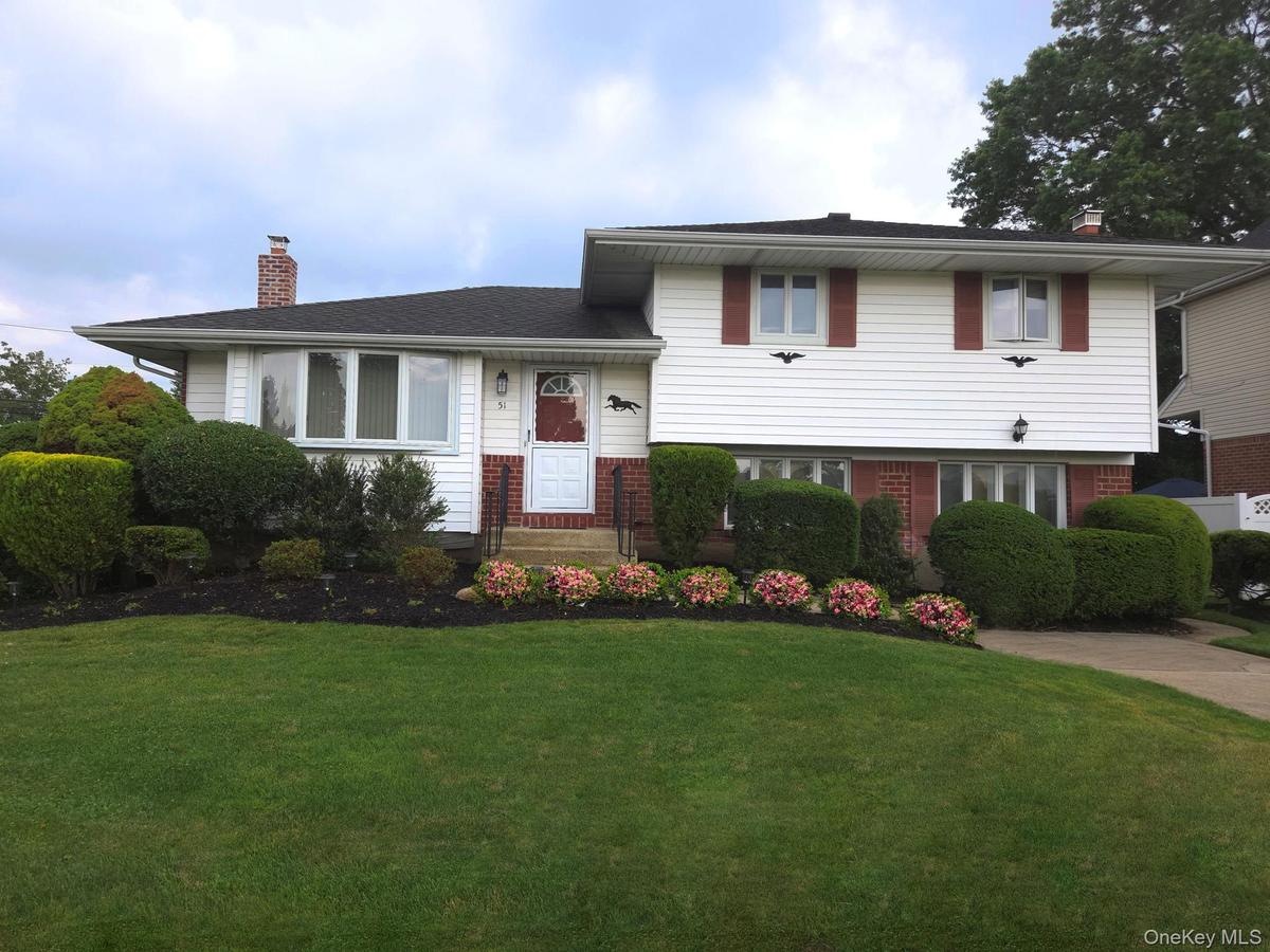 Split-level residence featuring white siding, a dark shingle roof, and a red front door