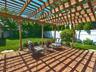 Brick paver patio featuring a wooden pergola with translucent roofing panels, surrounded by a manicured lawn, mature shrubs, and fencing