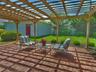 Brick paver patio featuring a wooden pergola with translucent roofing panels, surrounded by a manicured lawn, mature shrubs, and fencing